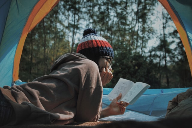 a young selective student reading book inside his tent on the woods