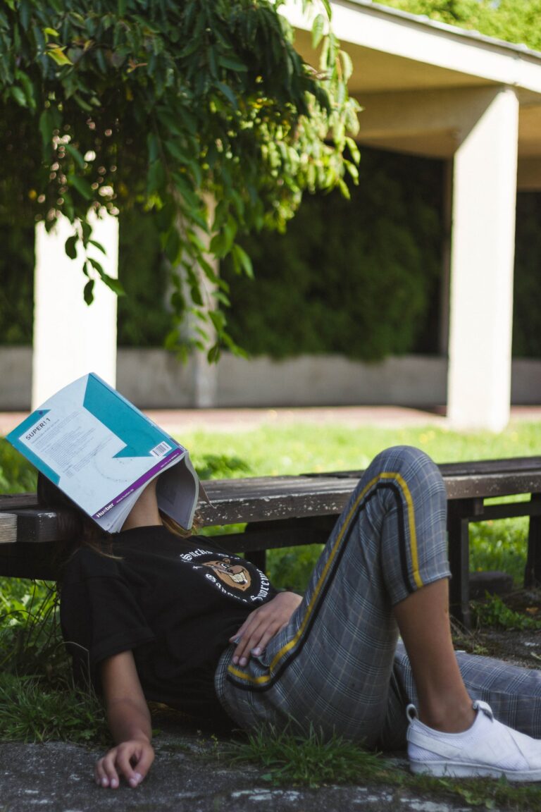 a selective student resting beneath a tree with her book on her face